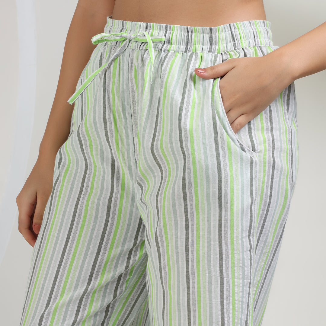 A close-up of a person wearing striped lounge pants with vertical stripes in white, gray, and lime green, featuring an elastic drawstring waist and side pockets.