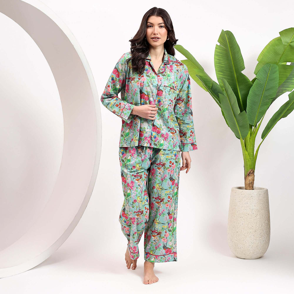 Woman wearing floral print pajamas for women, showcasing a vibrant floral design with soft fabric, standing by a decorative plant.