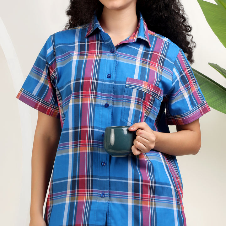 A person wearing a short-sleeve plaid button-up shirt in bright blue with pink, purple, white, and yellow stripes 