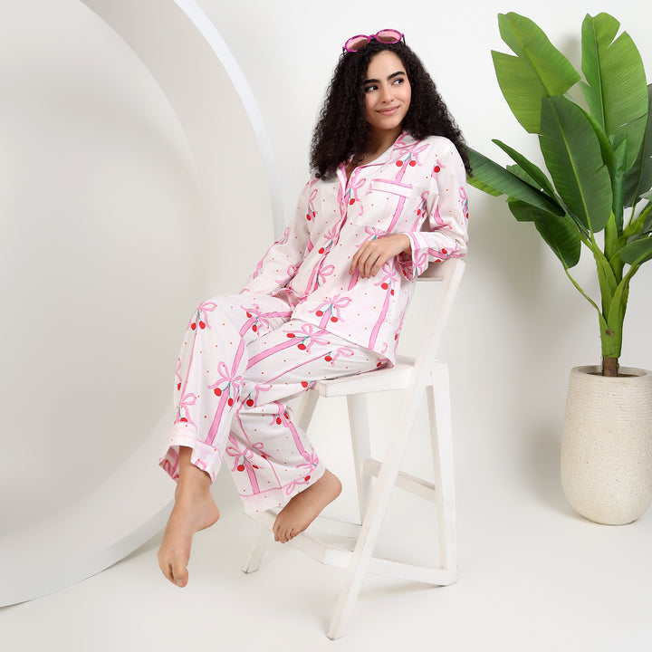 Woman sitting in a chair wearing Women's Organic Cotton Holiday Pajama Set - White & Pink Bow Print, showcasing comfort and style.