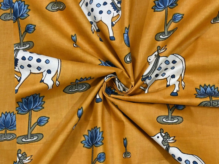 Mustard Indian cotton fabric showing white cows and blue lotus motifs