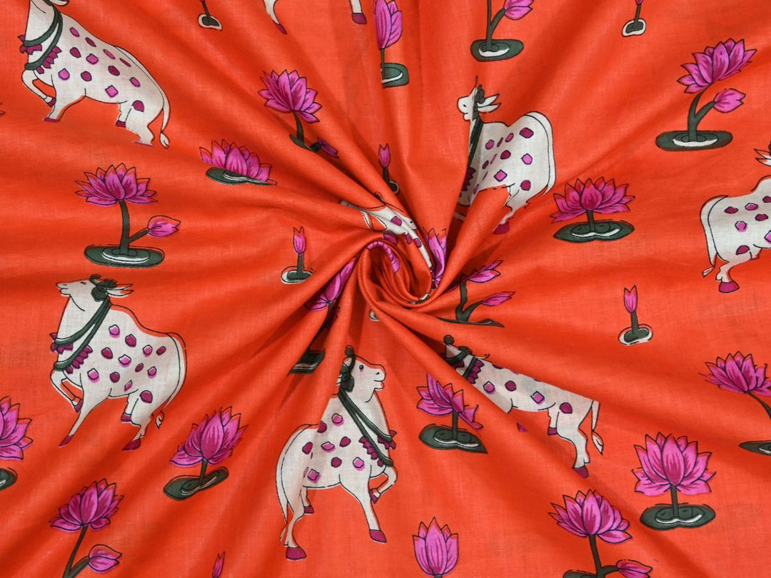 Orange Indian cotton fabric showing white cows with pink spots and lotus flowers