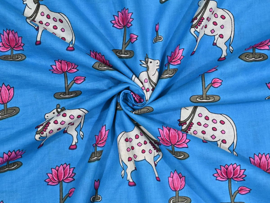 Blue Indian cotton fabric showing white cows with pink spots and lotus flowers