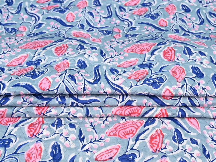 Close-up of dusty blue quilted fabric with pale pink accents and white outlines