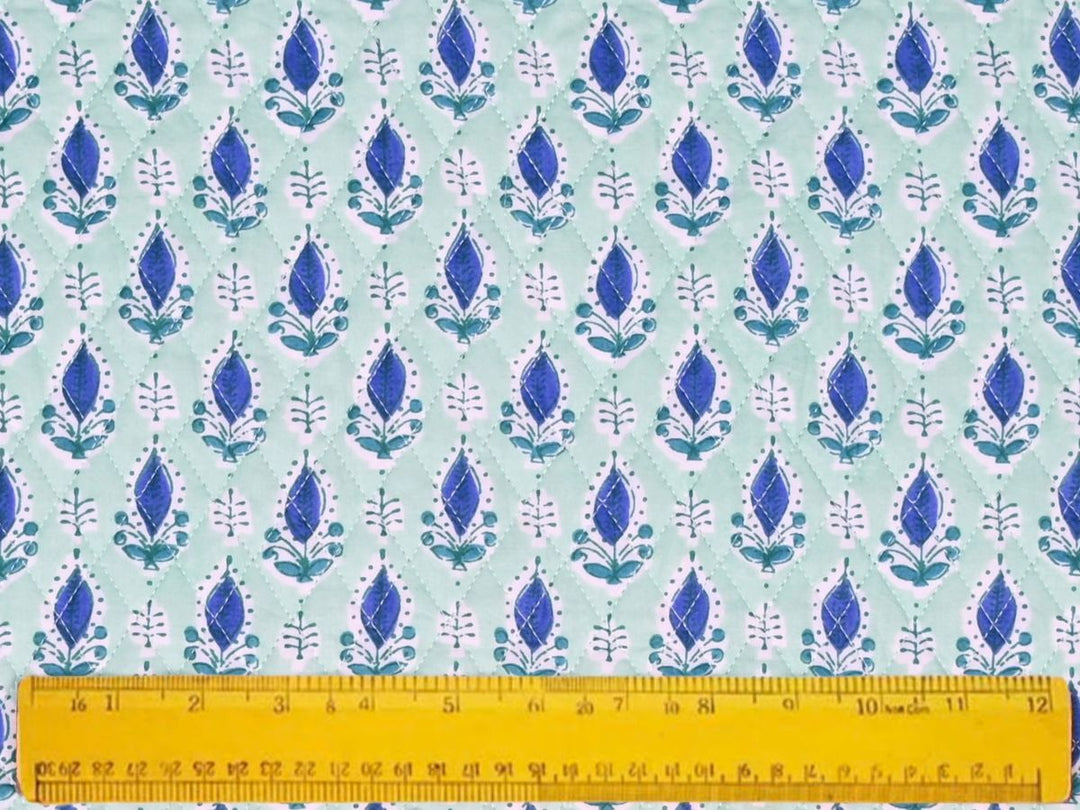 Close-up of mint green quilted fabric with diamond stitch lines and white fern sprigs