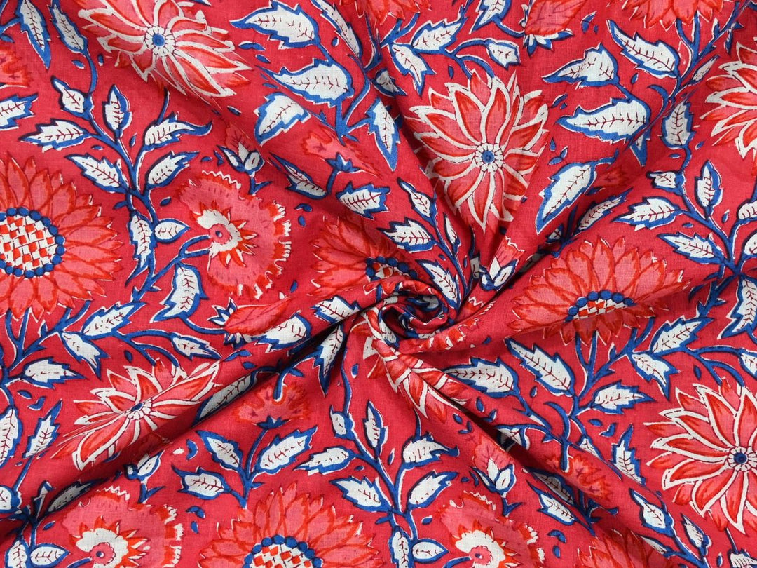 Red cotton fabric showing pink and red sunburst flowers with blue foliage