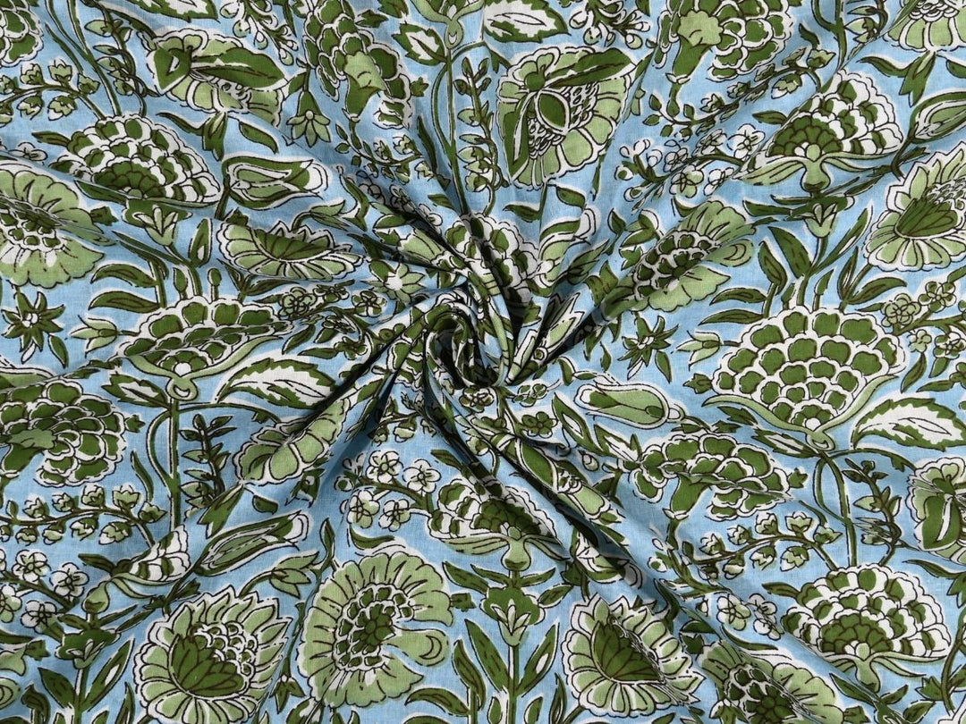 Light blue cotton fabric showing dense green peony and poppy blooms
