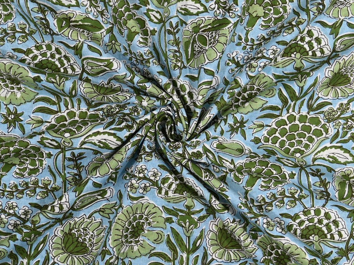 Light blue cotton fabric showing dense green peony and poppy blooms