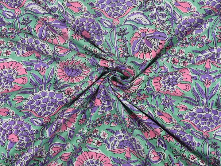 Green cotton fabric showing dense purple and pink floral block print