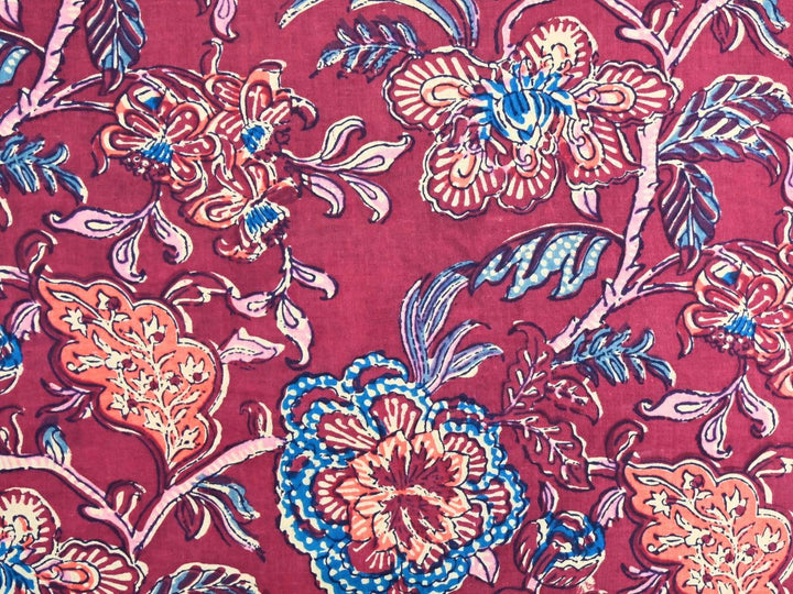 Deep red cotton fabric showing coral peony blooms with blue floral accents
