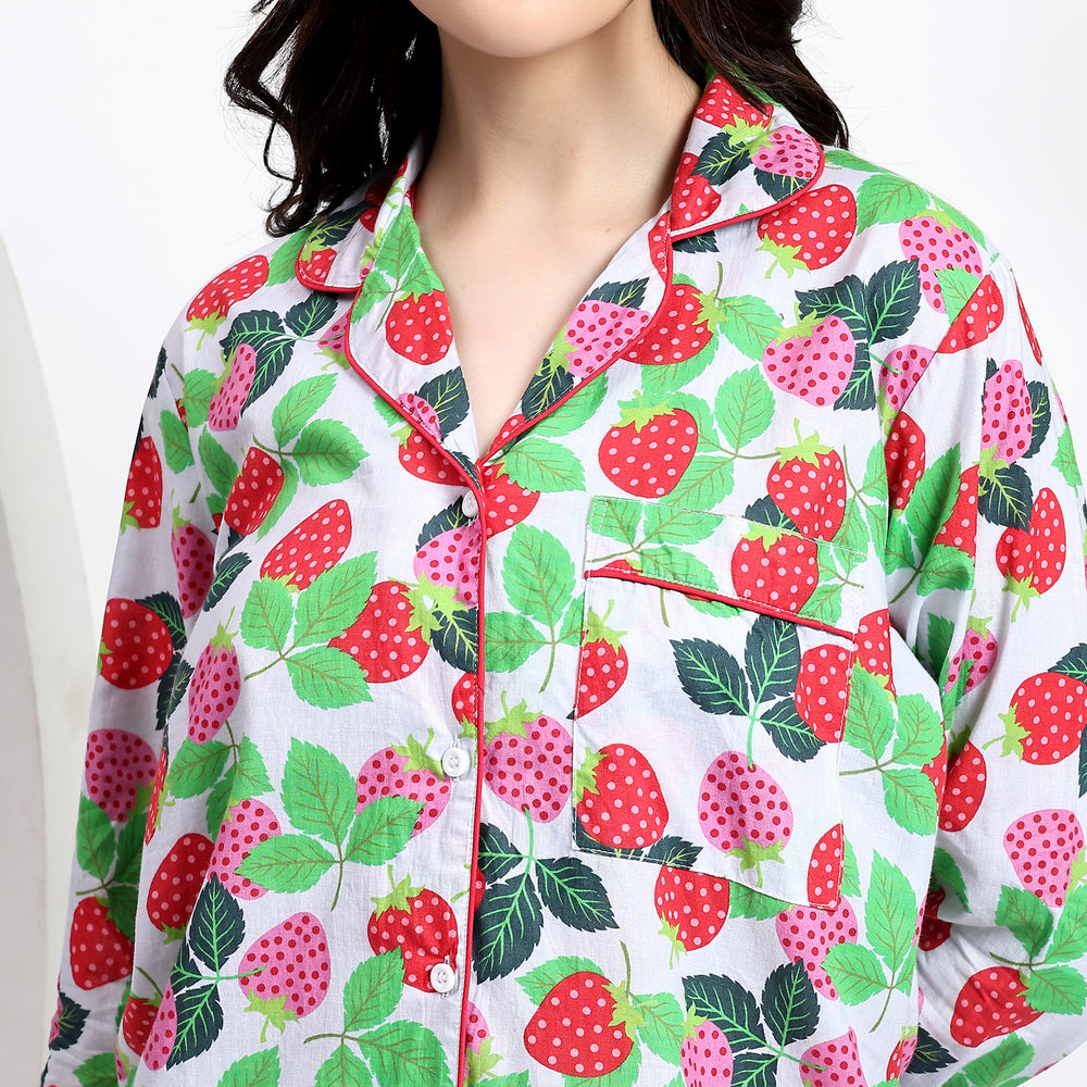 Close-up of white cotton pj set with front pocket and pink-red strawberry print detailing.