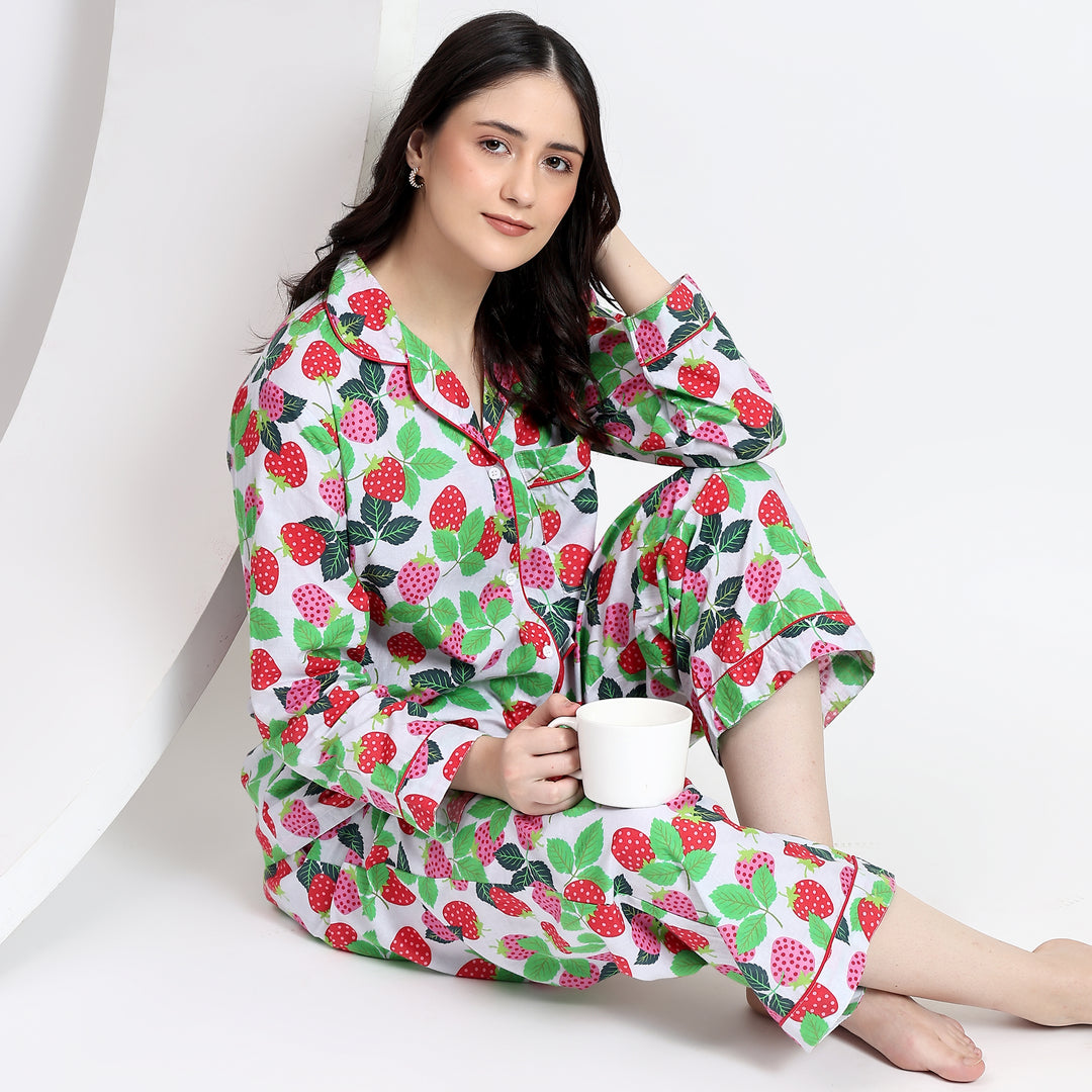 Sitting view of white cotton pajama set with pink and red strawberry print, featuring a front pocket and relaxed fit.